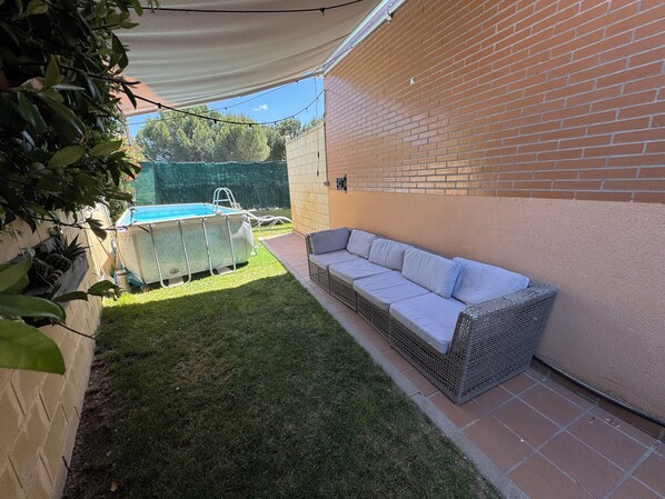 A backyard with a swimming pool, a wicker sofa, and a brick wall.