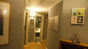 A hallway with wooden flooring, a door leading to a bedroom, and a small table with a decorative item. - Lux 2 Bed in Canary Wharf Close to Excel & O2 (London)