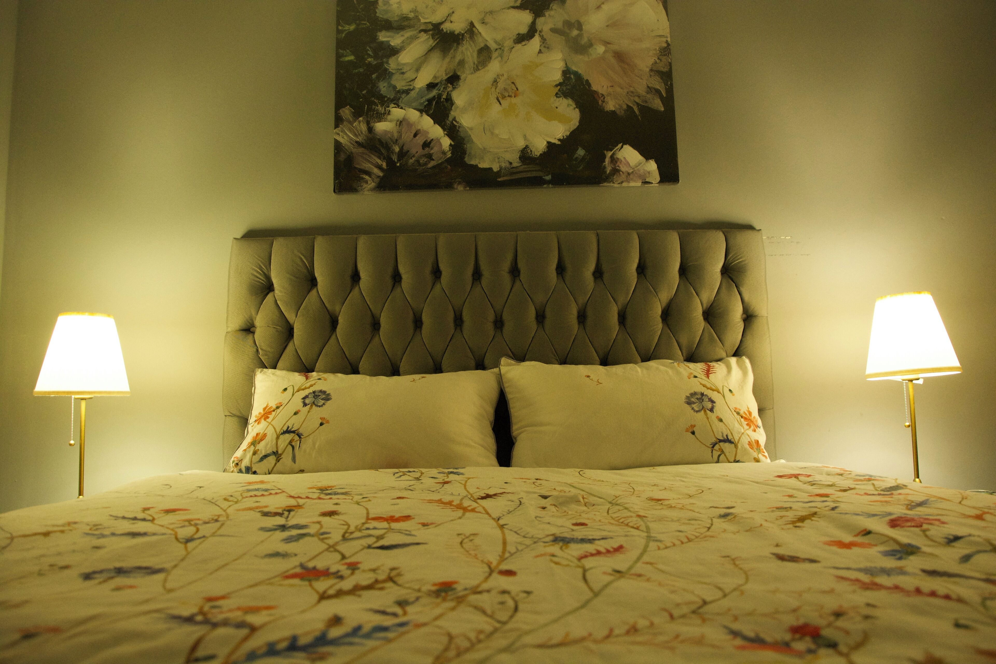 A bedroom with a tufted headboard, floral bedspread, and two bedside lamps.