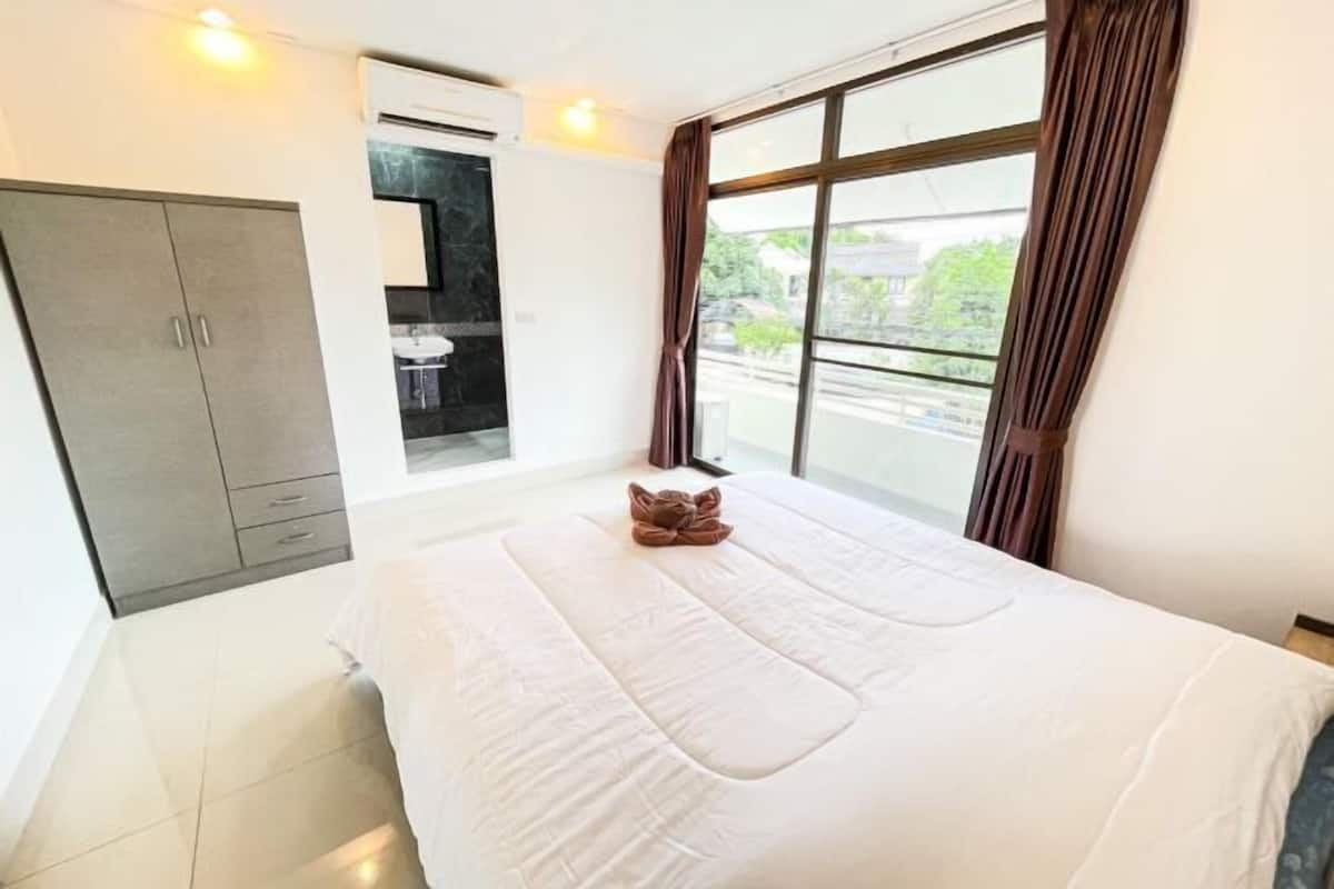 Ein Hotelzimmer mit Bett, Schrank, einem Fenster mit Vorhängen und Blick nach draußen.