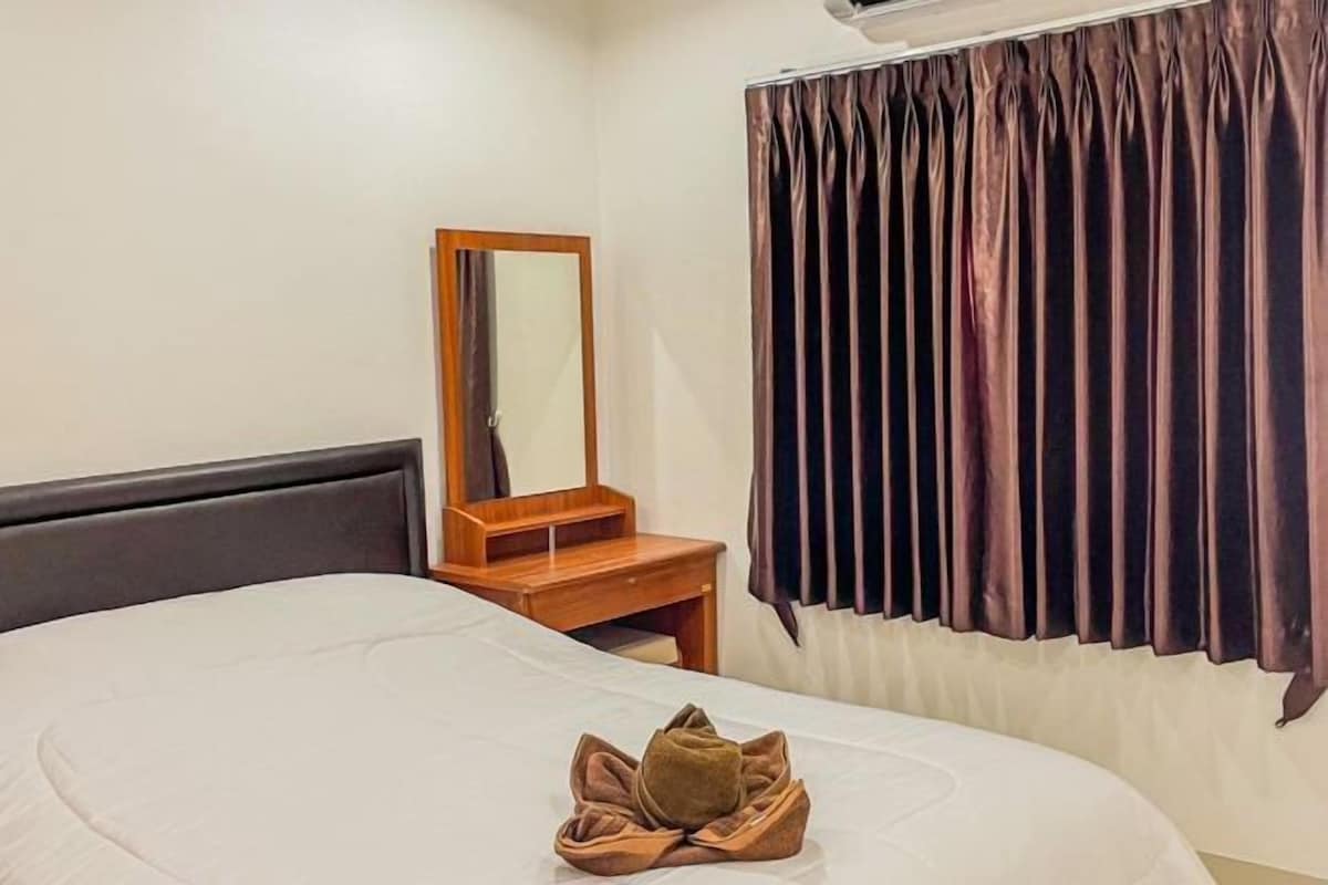 A hotel room with a bed, a wooden nightstand, a mirror, and a window with curtains.