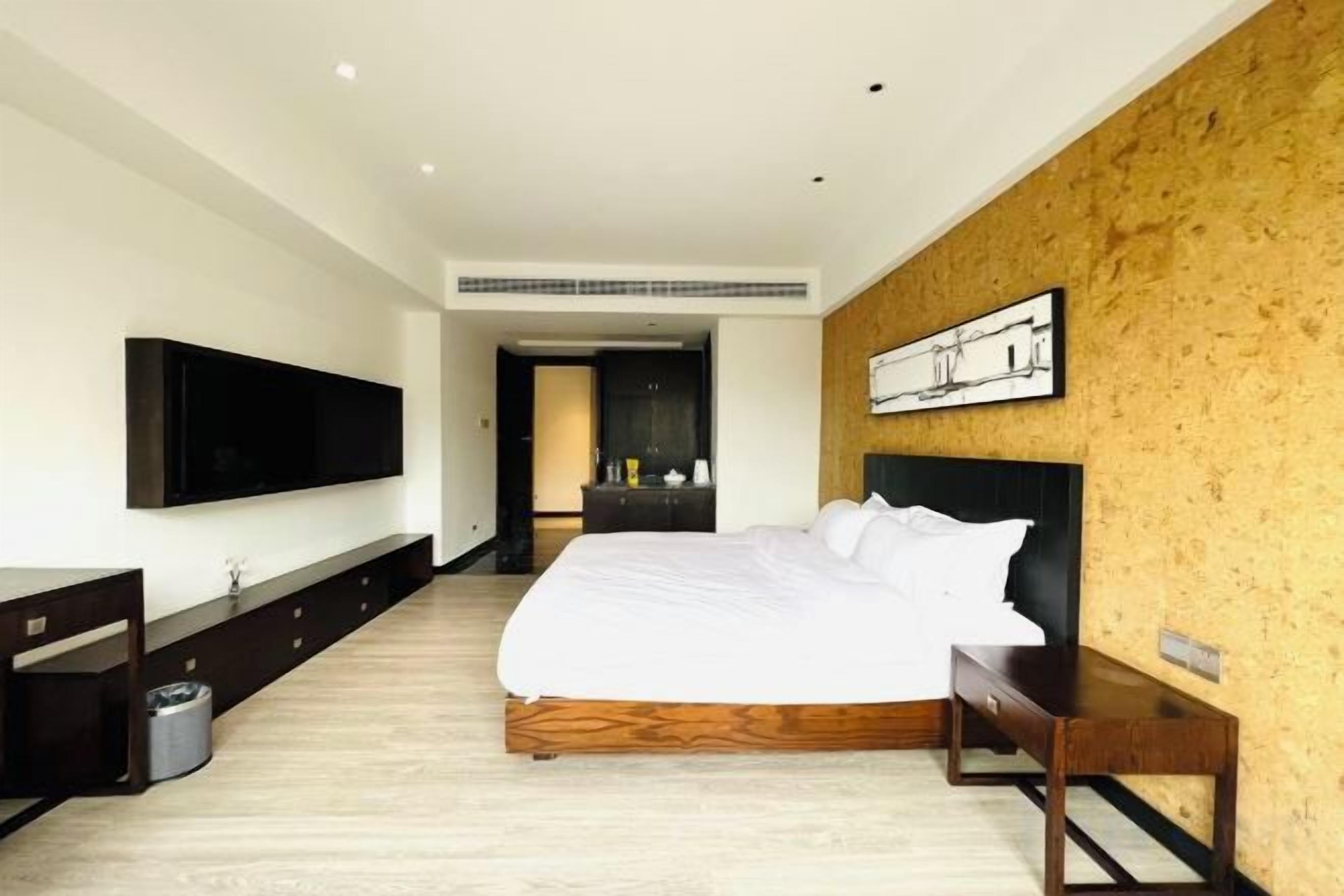 A modern bedroom with a large bed, a flat-screen TV, a wooden headboard, and a painting on the wall.