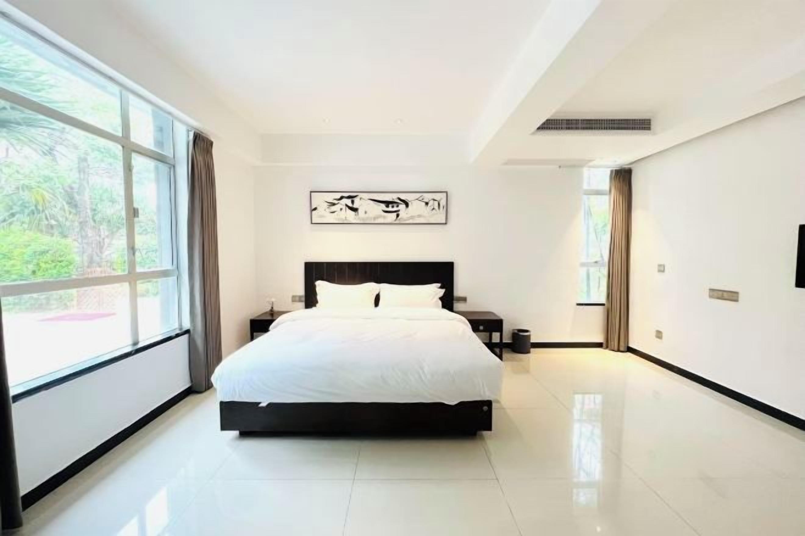 Une chambre moderne avec un grand lit, une table de chevet, une œuvre d’art accrochée au mur et une fenêtre avec des rideaux.