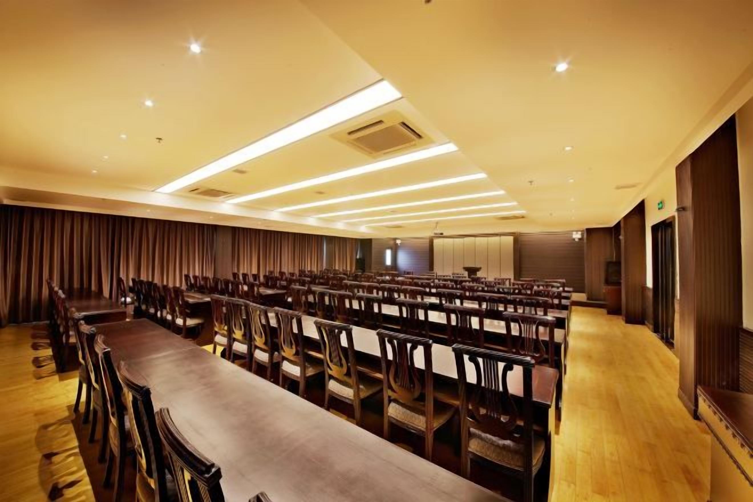 A conference room with rows of chairs and a long table, equipped with ceiling lights and a large screen.