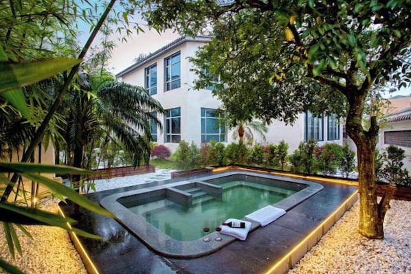 A hot tub in a landscaped garden with a building in the background.