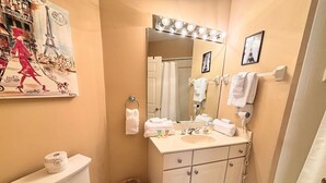 A bathroom with a toilet, sink, mirror, and a painting of a cityscape.