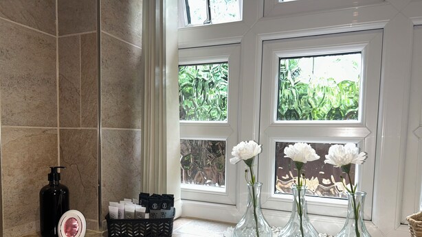 A bathroom with a marble countertop, a black soap dispenser, a tissue box, and three vases with white flowers. - Claverley Hideaway Apartment Bridgnorth (Wolverhampton)