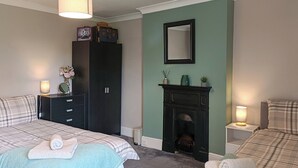 Un dormitorio con dos camas, un armario, una chimenea y un espejo en la pared.