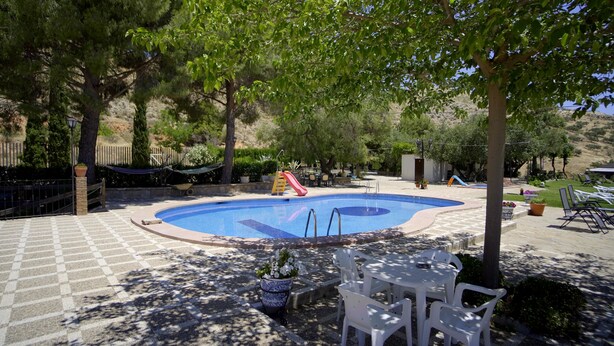 A swimming pool with a slide, surrounded by trees and outdoor furniture. - Accommodation LA GUITARRA ANDALUZA  (Loja)