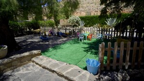 A fenced backyard with artificial grass, a wooden play area, and a stone wall. - Accommodation LA GUITARRA ANDALUZA  (Loja)