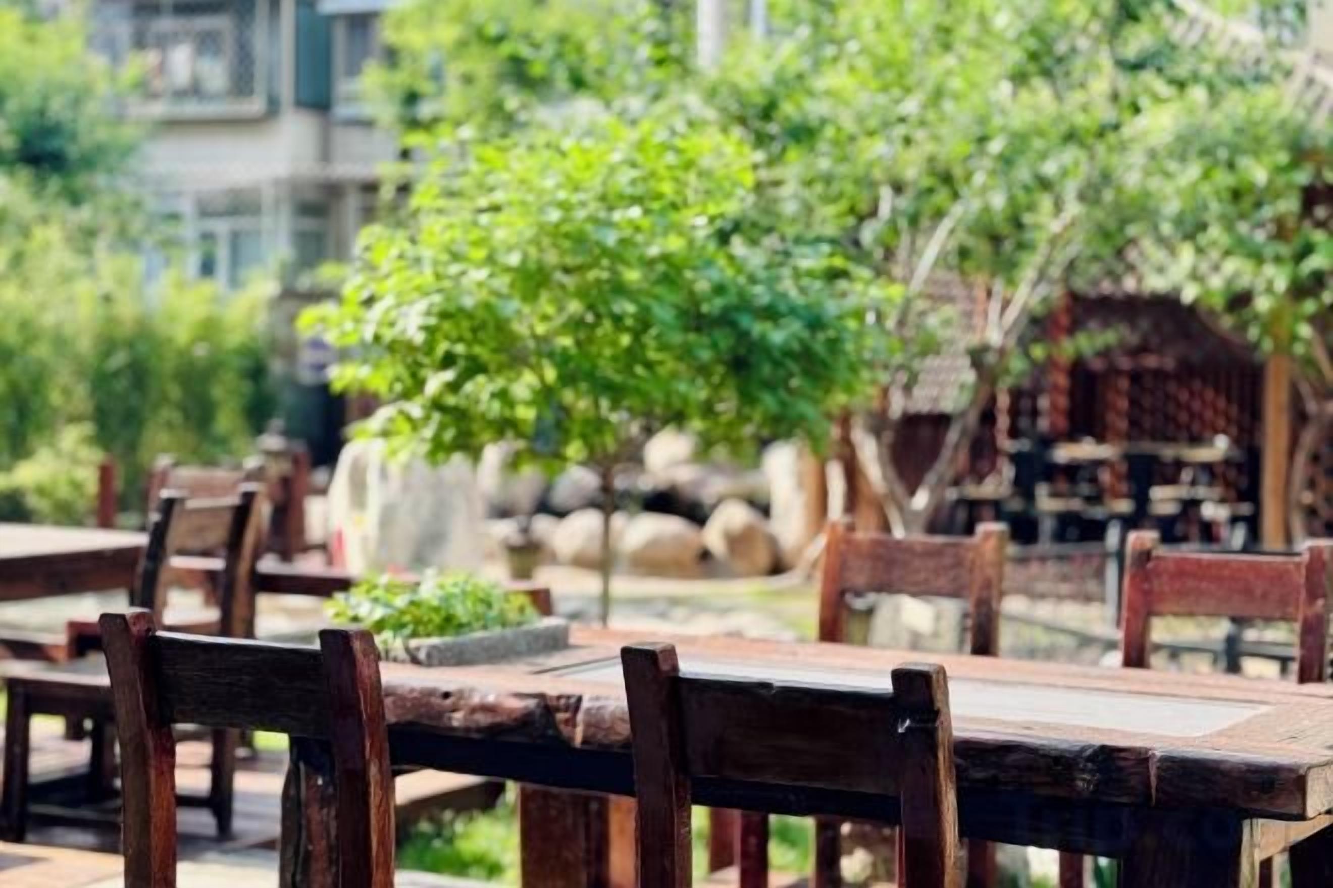 Mesas y sillas de madera al aire libre en un jardín con muros de piedra y follaje.