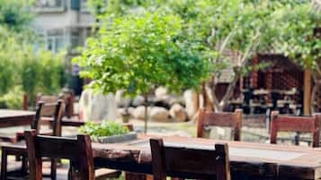 Mesas y sillas de madera al aire libre en un jardín con muros de piedra y follaje.