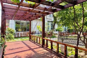 A wooden deck with a railing, surrounded by greenery and a building in the background. - Wanshang Ruyi Hotel (Beijing Lugu East Street) (Beijing)