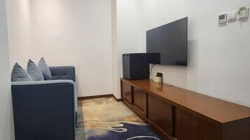 Una sala pequeña con un sofá, un televisor montado en la pared, una consola de madera y un tapete estampado.