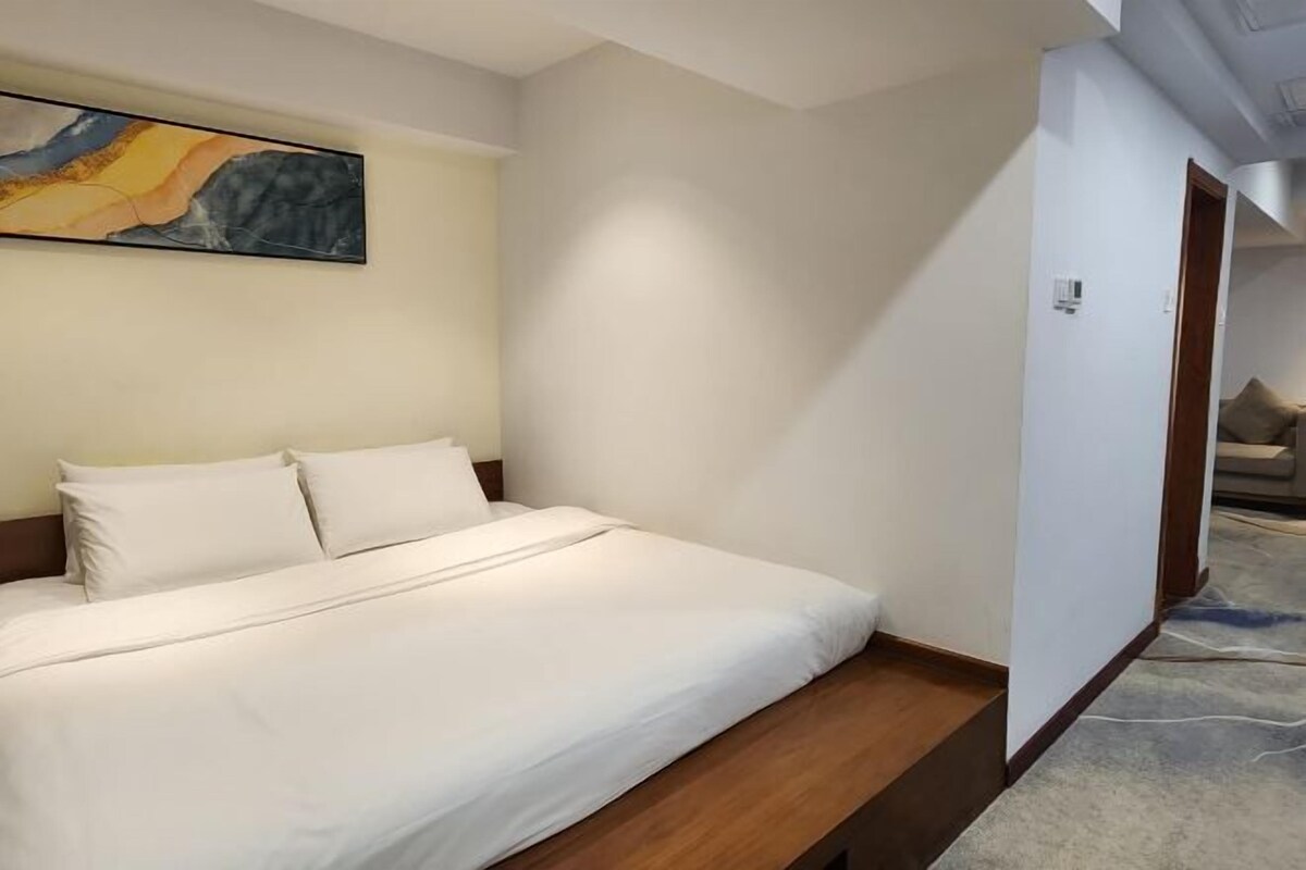 Quarto de hotel com uma cama, um quadro na parede e uma porta que dá para outro espaço.