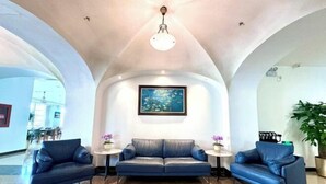 Eine Lobby mit einem blauen Ledersofa, zwei Beistelltischen, einem gerahmten Gemälde und einer Topfpflanze.