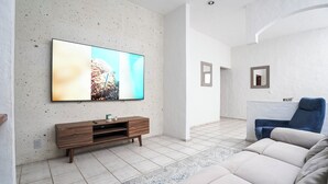 Una sala de estar moderna con una televisión de pantalla plana montada en una pared texturizada, un mueble de madera para entretenimiento, un sofá color beige y un sillón azul.
