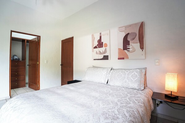 Une chambre à coucher avec un lit, une table de chevet, une lampe et deux tableaux abstraits accrochés au mur.