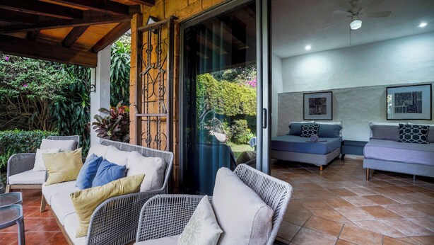 Un patio acogedor con mobiliario de mimbre, y una puerta corrediza de vidrio que da a un salón con un sofá y un ventilador de techo.