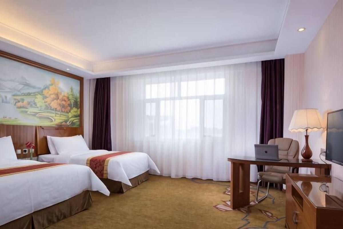 Hotellihuone, jossa on kaksi sänkyä, työpöytä kannettavalla tietokoneella, televisio ja taulu seinällä.