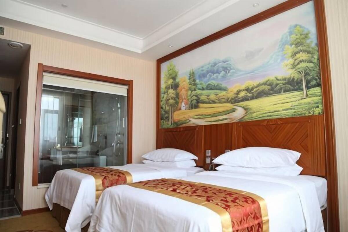 Hotellihuone, jossa on kaksi sänkyä, suuri ikkuna ja maisemamaalaus.