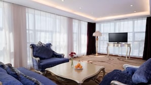 A modern living room with a large TV, plush blue sofas, and a coffee table with fruit. - Vienna International Hotel (Tongliao Kerqin) (Tongliao)