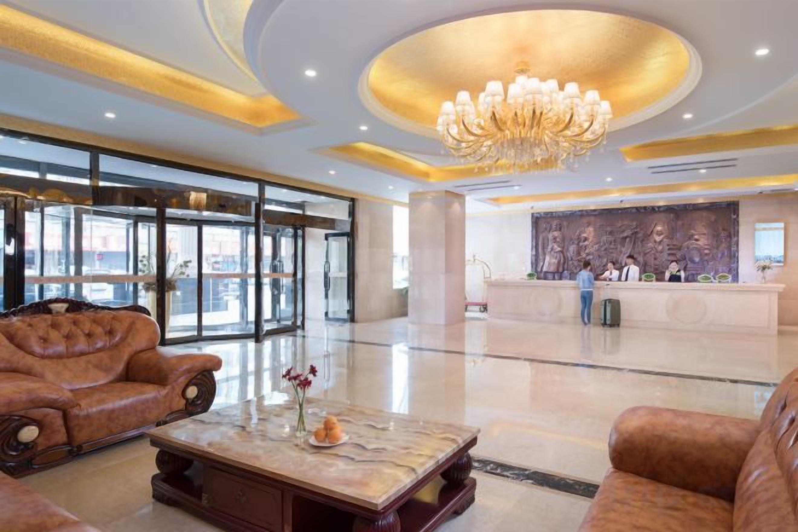 A hotel lobby with a reception desk, leather sofas, a marble coffee table, and a chandelier.