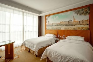 Habitación de hotel con dos camas, una mesita de noche, una mesa y un cuadro de un paisaje urbano en la pared.