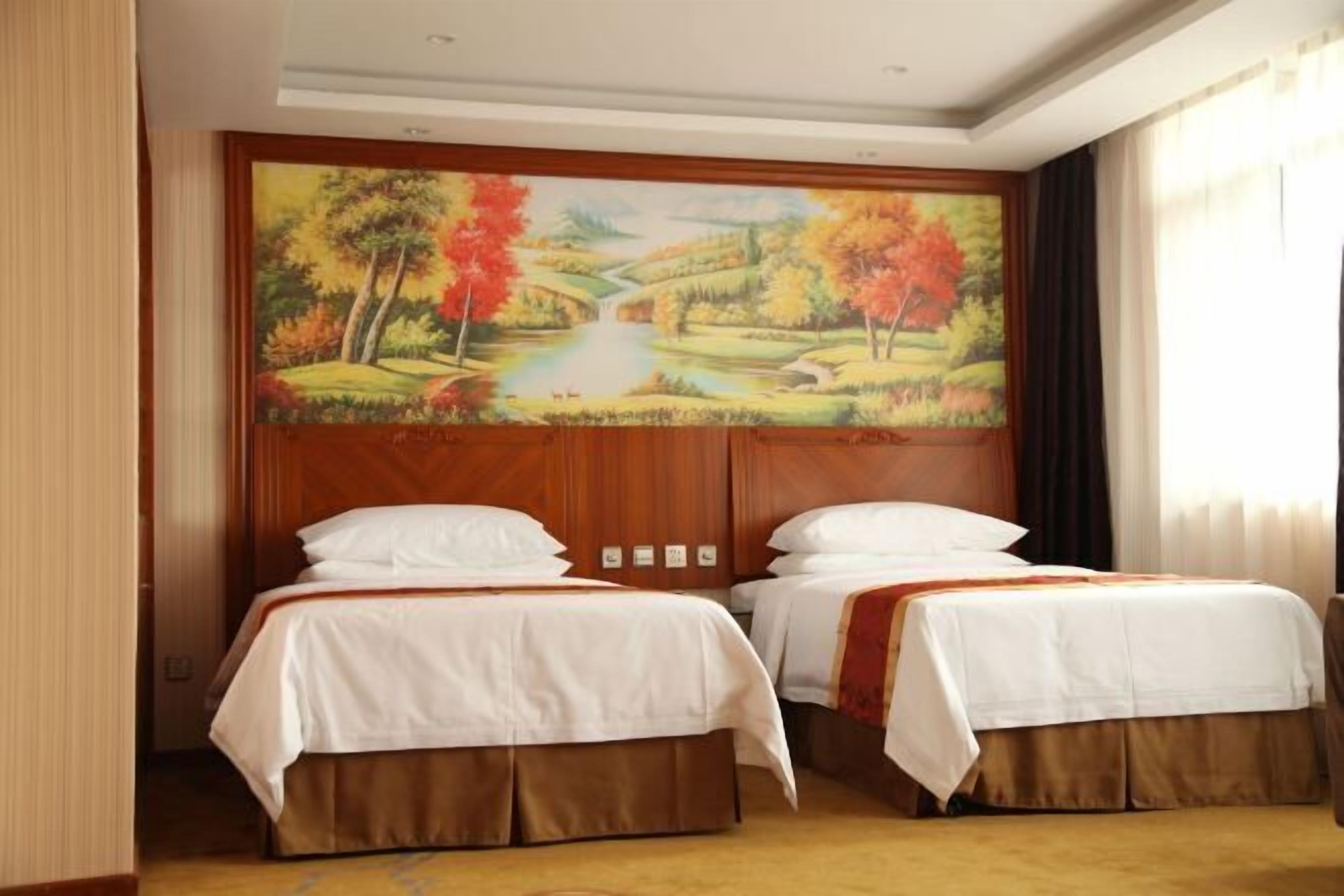 A hotel room with two beds, a large painting of a landscape on the wall, and a view of a body of water.
