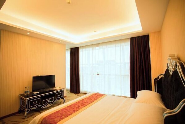 Quarto de hotel com uma cama, televisão num aparador, janela com cortinas e um guarda-roupa.