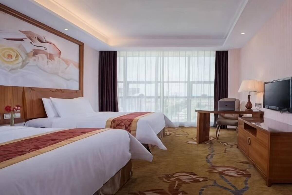 Hotellihuone, jossa on kaksi sänkyä, televisio, työpöytä lampun kanssa ja suuri ikkuna.