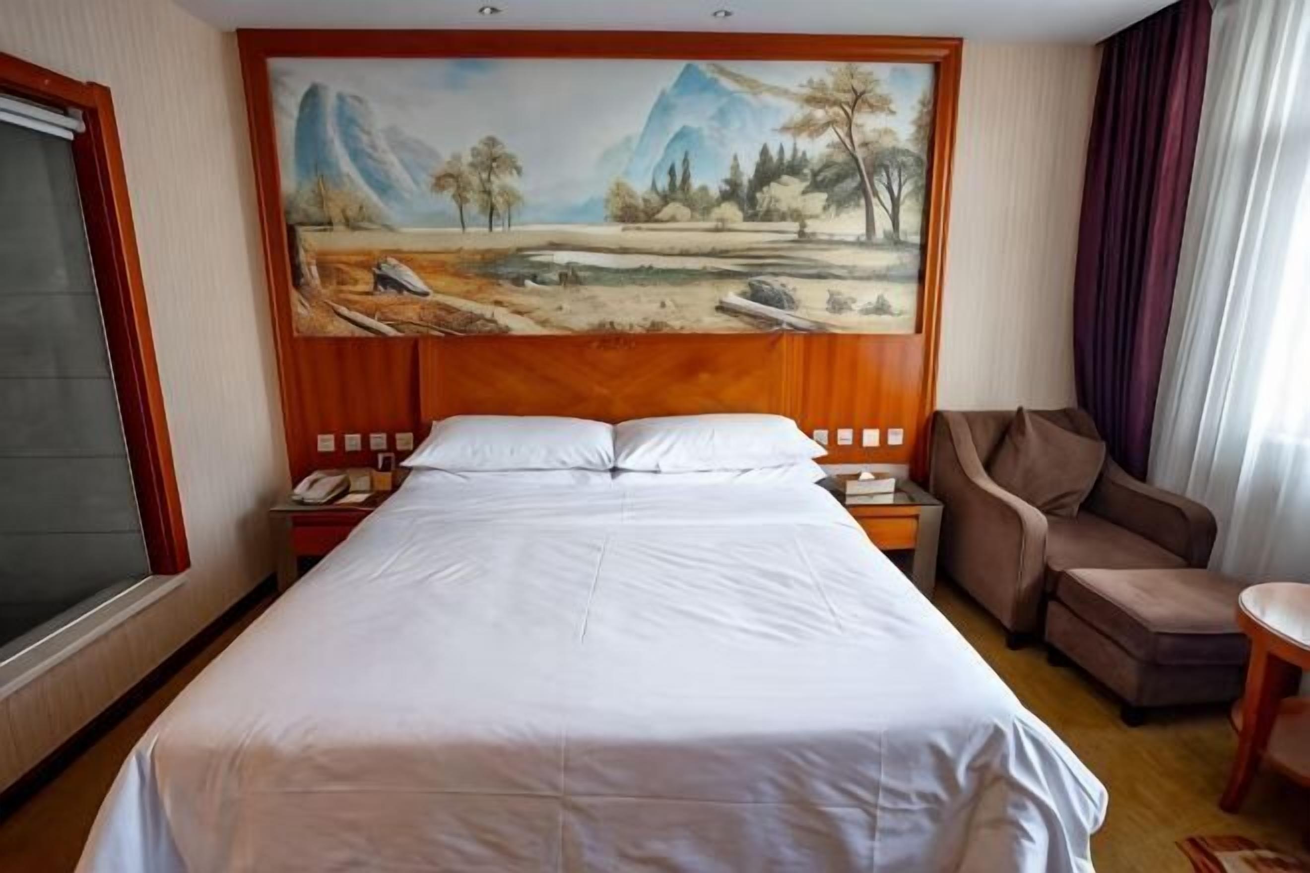 Une chambre d’hôtel avec un grand lit, un tableau au mur, un bureau et une chaise.