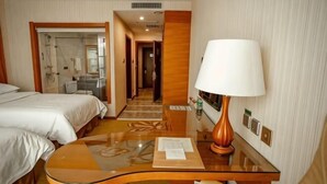 A hotel room with a bed, a desk with a lamp, a mirror, and a view of a hallway. - Vienna International Hotel (Tongliao Kerqin) (Tongliao)