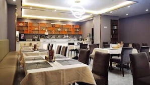 A restaurant with multiple dining tables and chairs, a kitchen in the background, and a modern ceiling design. - Vienna International Hotel (Tongliao Kerqin) (Tongliao)