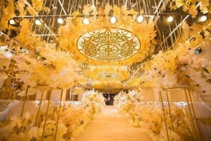 Um corredor com um caminho dourado, ladeado por arranjos florais brancos e um desenho decorativo no teto.