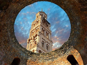 Une tour historique dotée d’une horloge, vue à travers une arche circulaire en pierre.