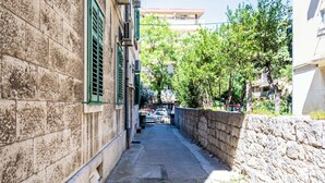 A narrow stone-paved alleyway flanked by buildings with green shutters and air conditioning units. - Traditional Dalmatian Apt, 3 min Walk to Beach (Split)