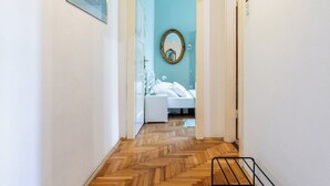 A hallway with a wooden herringbone floor, a framed picture on the left, and a bed with a mirror in the background. - Traditional Dalmatian Apt, 3 min Walk to Beach (Split)