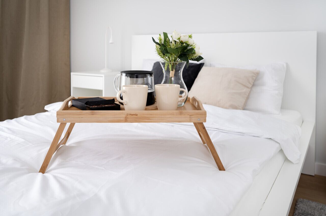 Une table de chevet en bois sur laquelle se trouvent une cafetière, deux tasses et un vase rempli de fleurs.