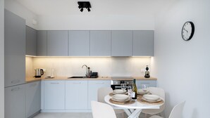 Una cucina moderna con mobili grigi, un tavolo da pranzo bianco con quattro sedie e una sveglia appesa al muro.