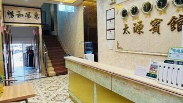 A hotel reception area with a marble counter, a staircase, and a wall with clocks.