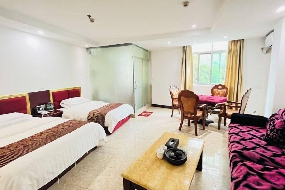 A hotel room with two beds, a dining table with chairs, a sofa, and a small table with a telephone and a bowl.