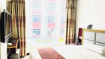 A hotel room with a bed, a television, a desk with a computer, and a window with curtains.