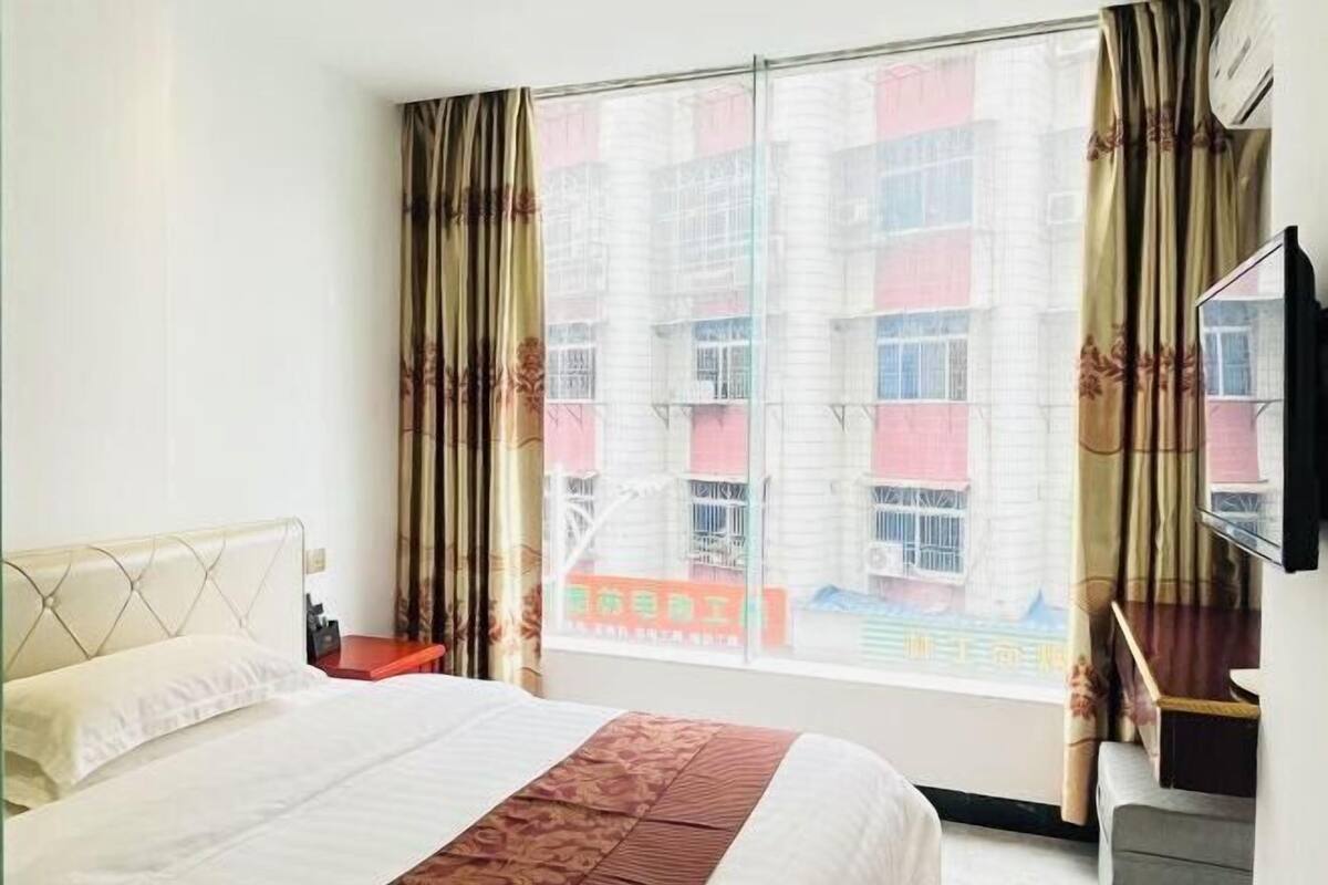 A hotel room with a bed, a desk, a chair, a TV, and a window with curtains.