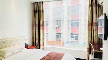 A hotel room with a bed, a nightstand, a desk, and a large window with curtains.
