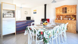 A dining area with a table set for four, surrounded by white chairs, a wooden cabinet with glass doors, and a blue sofa. - Les PerceNeige - Maison 85 m² à Port-Bail-Sur-Mer (Portbail)