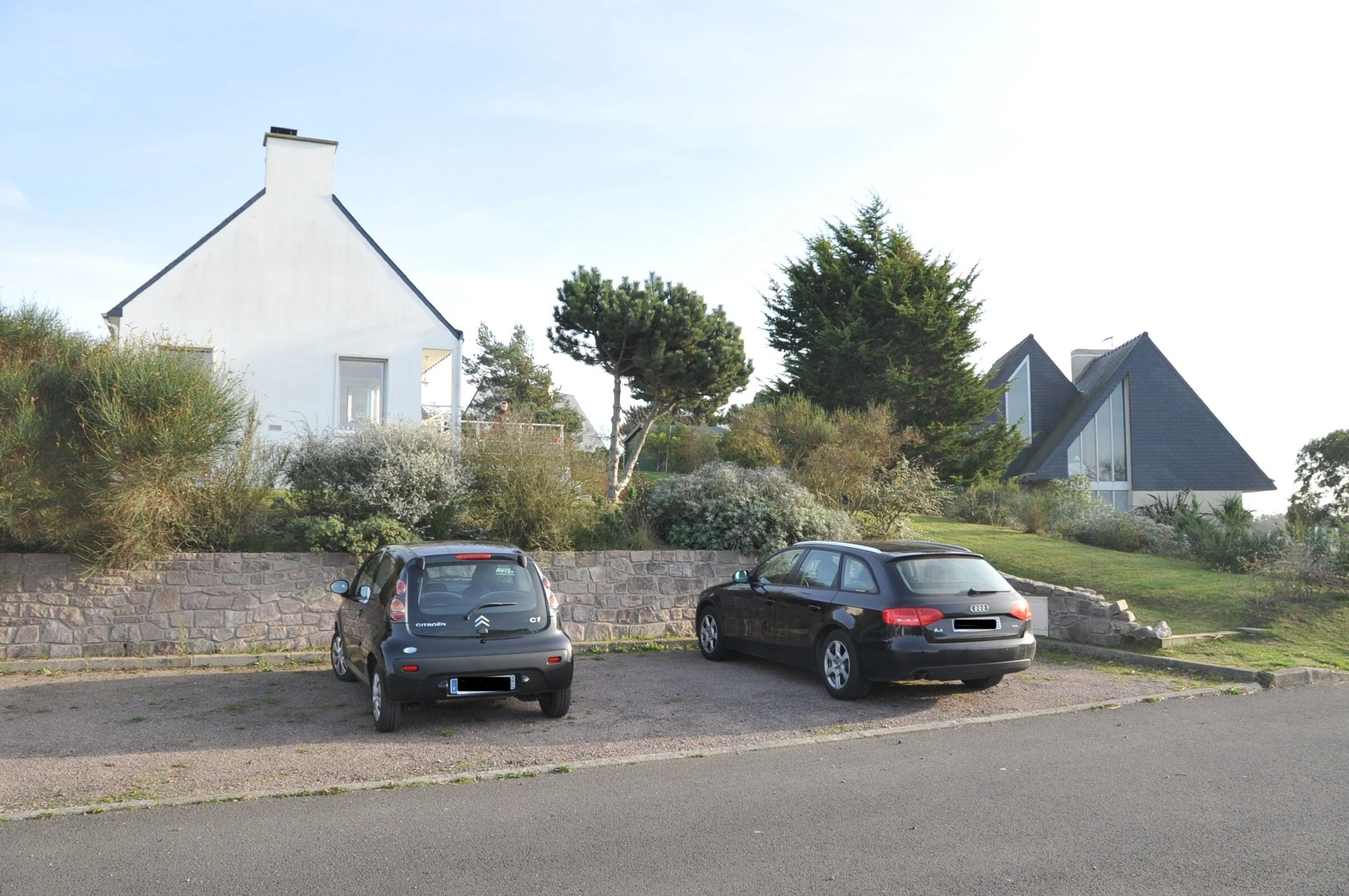 Zwei Autos stehen auf einer Auffahrt mit einer Steinmauer und einem Haus im Hintergrund.