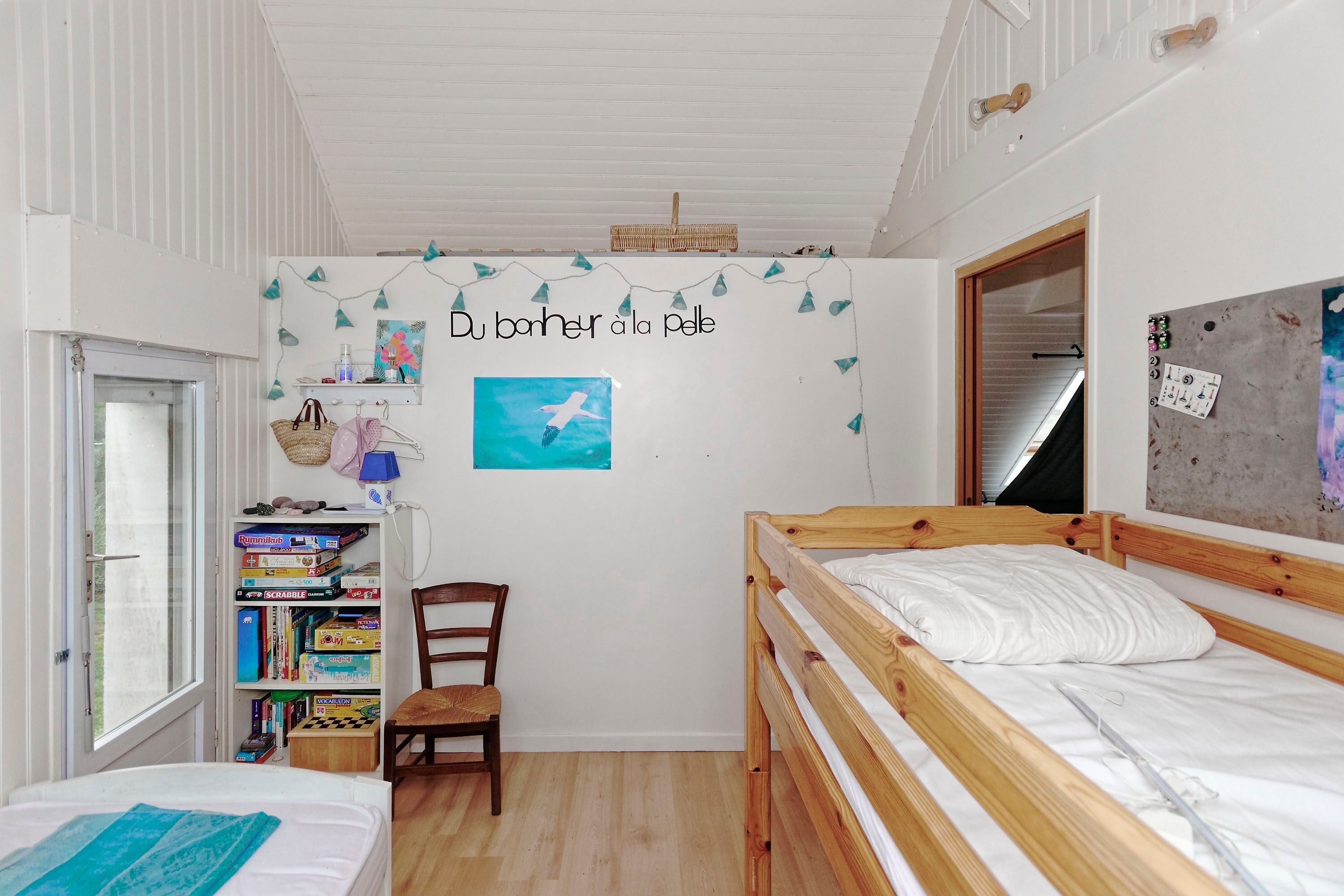 Ein Schlafzimmer mit Etagenbett, einer Bücherwand voller Gegenstände, einem Fenster und einer Wand mit einer Girlande und einem Gem älde.