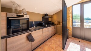 Una cucina moderna con forno integrato, piano cottura e cappa aspirante nera. Ci sono due barattoli di vetro sul forno e un asciugamano nero appeso alla porta del mobile. La cucina ha un'ampia finestra con vista sull'esterno.