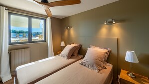 Una camera da letto con due letti, un ventilatore a soffitto, una finestra con tende e un comodino con una lampada.